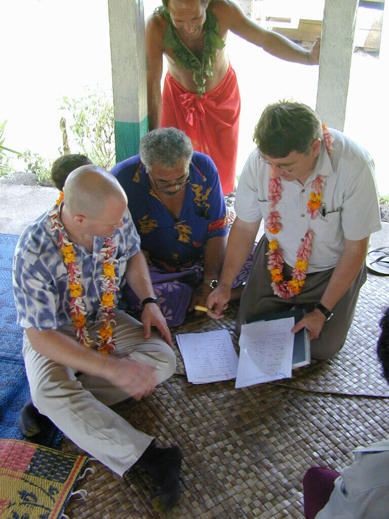Men discussing papers on a mat.