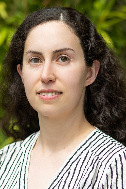 Woman in striped shirt with green foliage in the background.