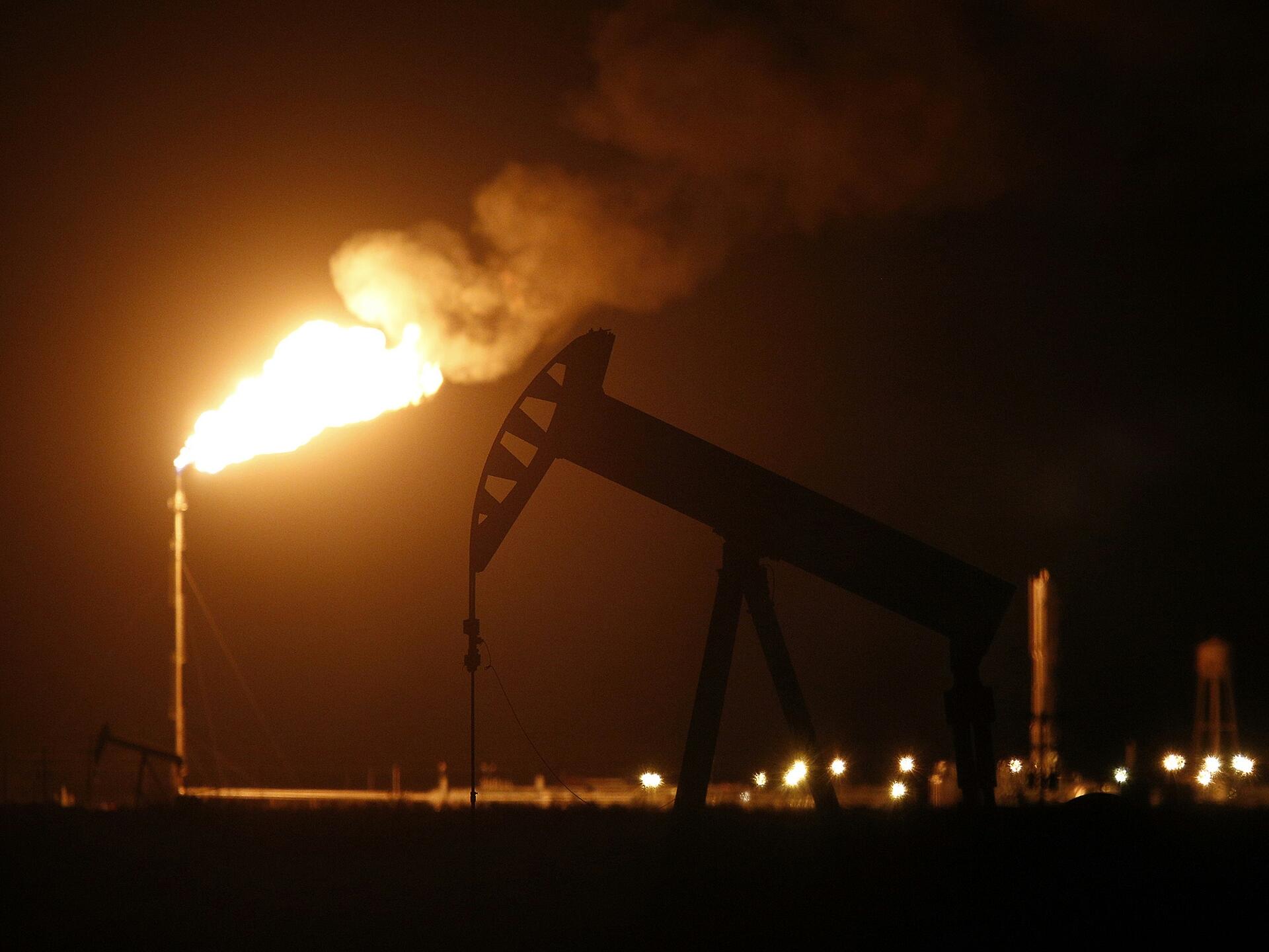 Flaring of natural gas in the Texas oil fields silhouettes an electric oil pump jack. Luke Sharrett/Bloomberg