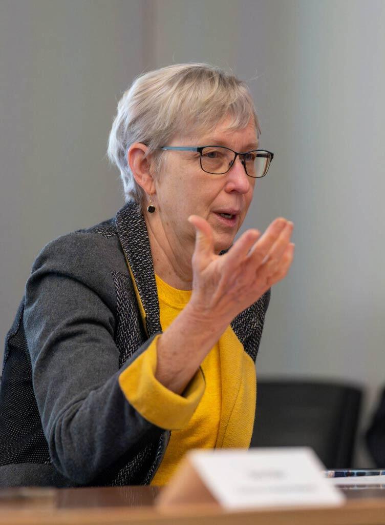 a woman with glasses and a yellow blouse gesturing while talking