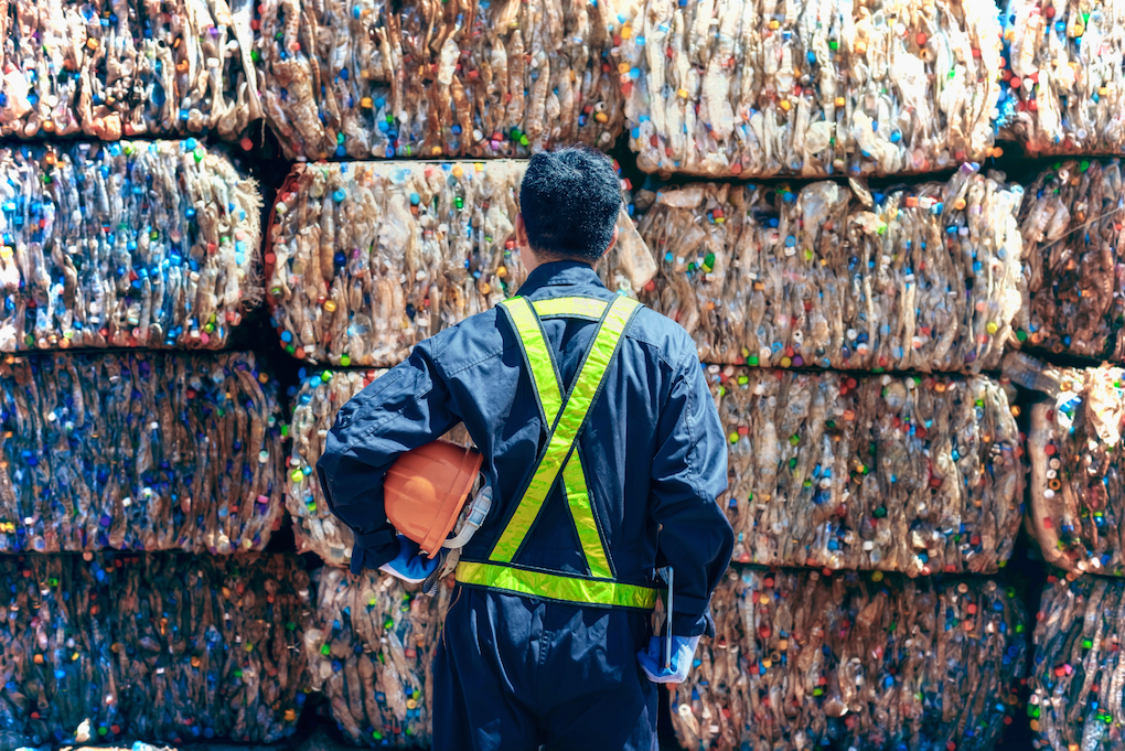 worker looks at bails of plastic